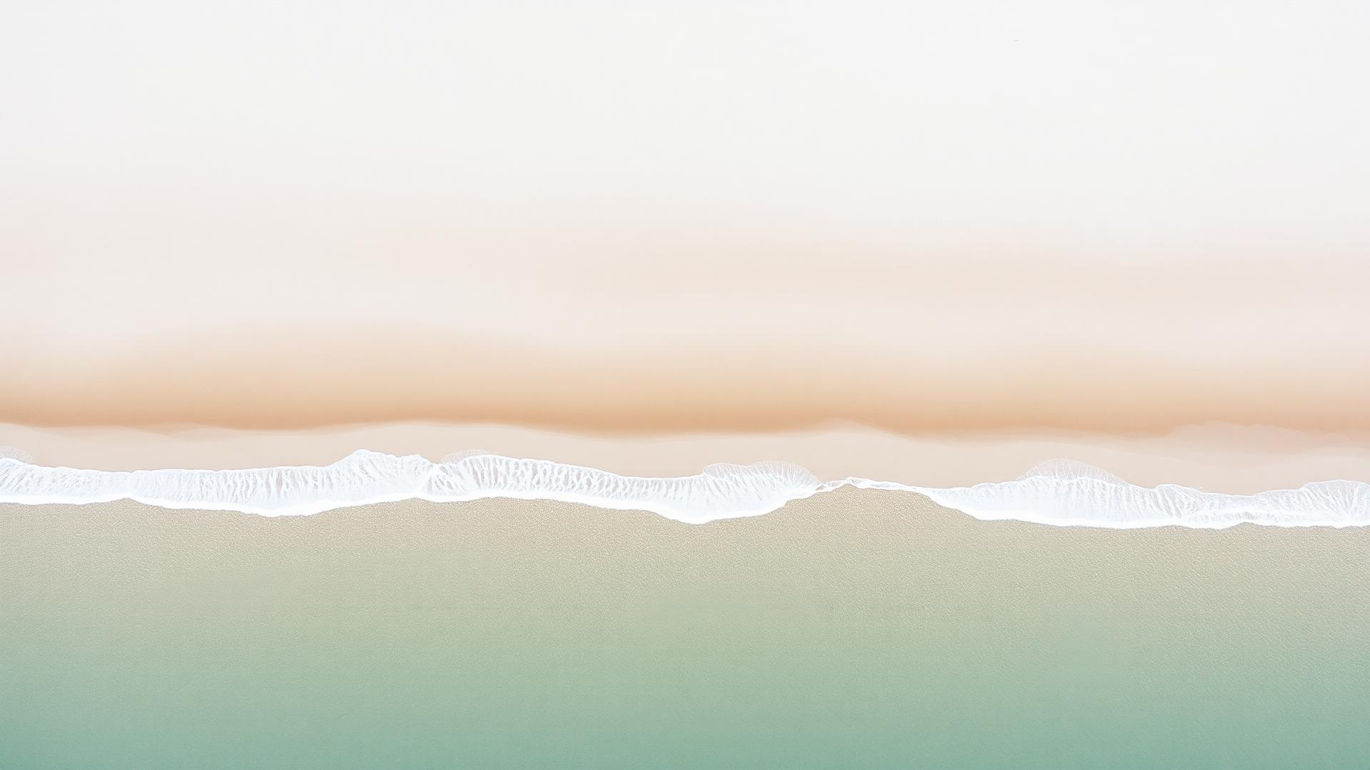 Aerial view of a calm shoreline where soft waves meet pale sand
